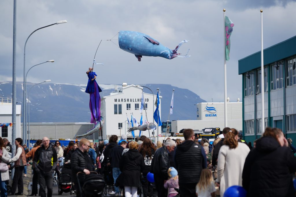 A stilt performer and a whale puppet entertain a crowd.