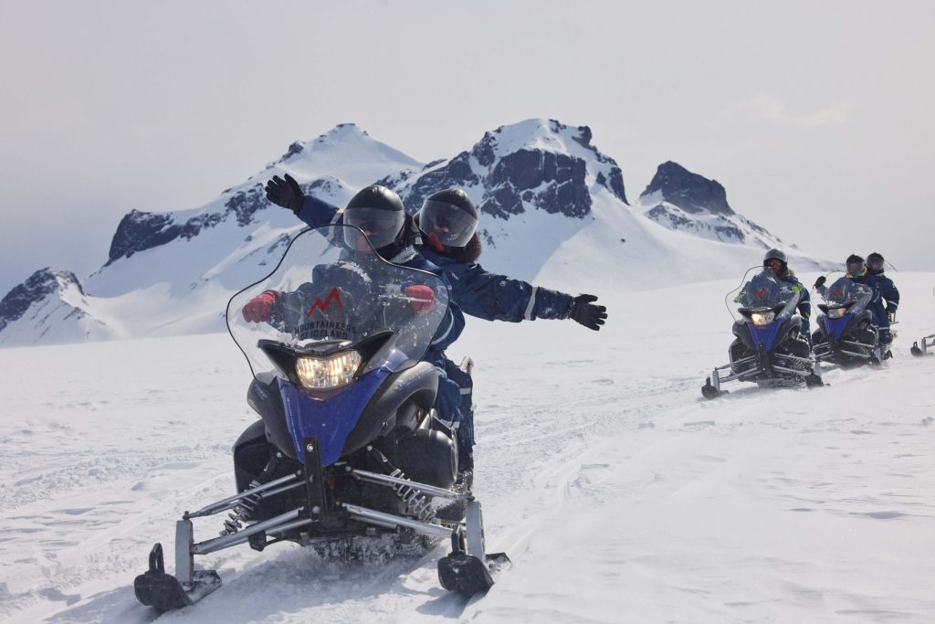 Destination management company in Iceland organizing a snowmobile experience on a glacier surrounded by snowy mountains.