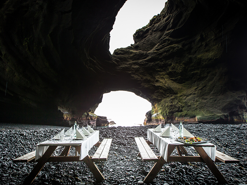 Event planning in Iceland with an outdoor dining setup inside a dramatic sea cave on a black pebble beach