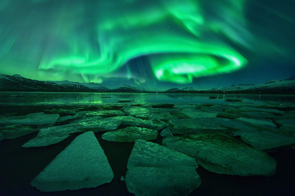 Iceberg floating in Jökulsárlón in Iceland with northern lights shining above.