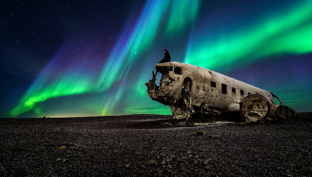 Northern lights glow above a plane wreck on a black-sand beach in Iceland.