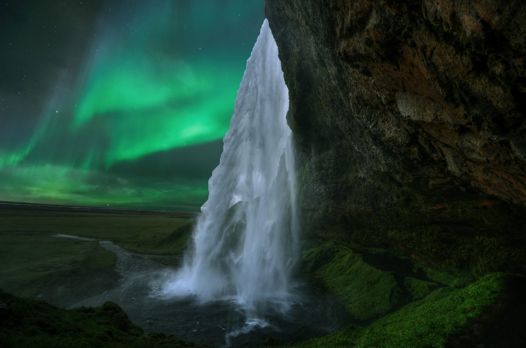 Northern lights glow behind Seljalandsfoss waterfall in southern Iceland.