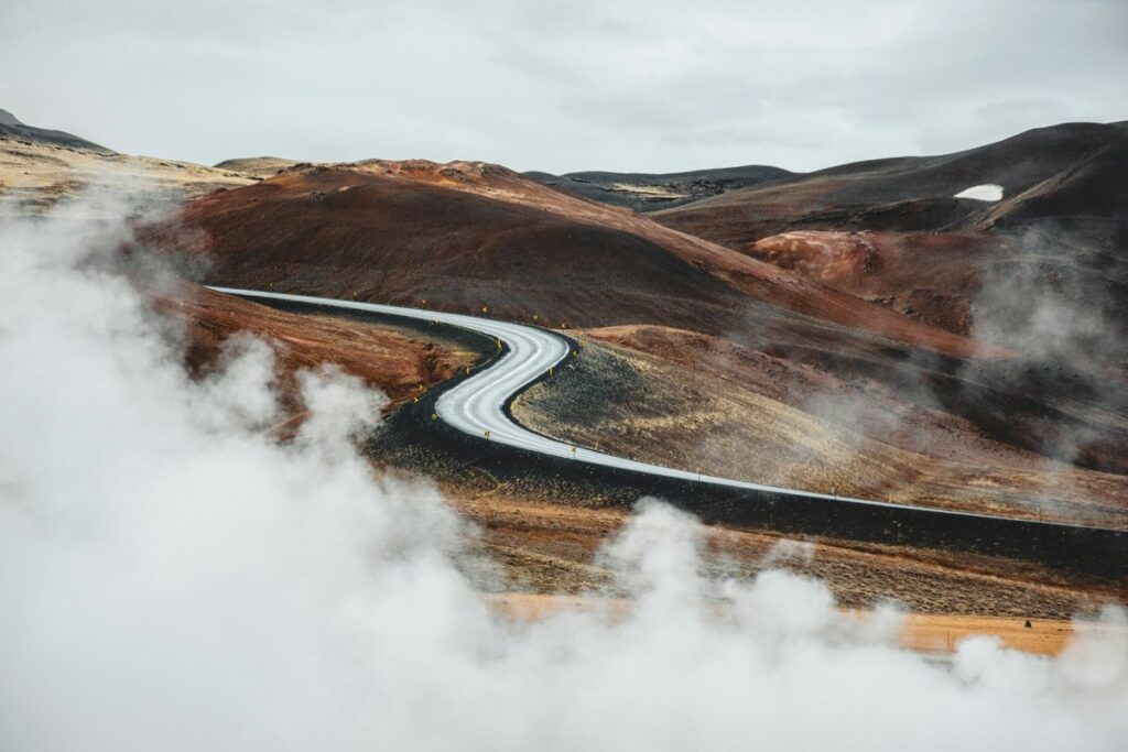 Winding road through Iceland’s rugged volcanic mountains, surrounded by mist and geothermal steam, showcasing the country’s dramatic natural landscape.