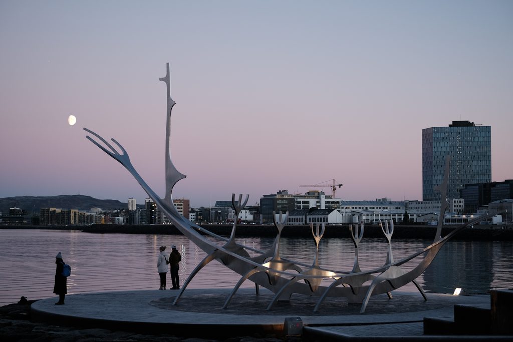 The Sun Voyager sculpture on Reykjavik’s waterfront at dusk, overlooking calm water and the city skyline beneath a pale moon.