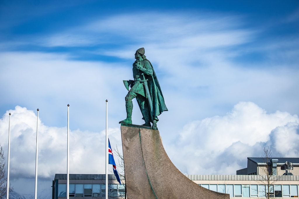 Statue of Leif Erikson in Reykjavik, Iceland, standing against a dramatic blue sky with an Icelandic flag flying nearby.